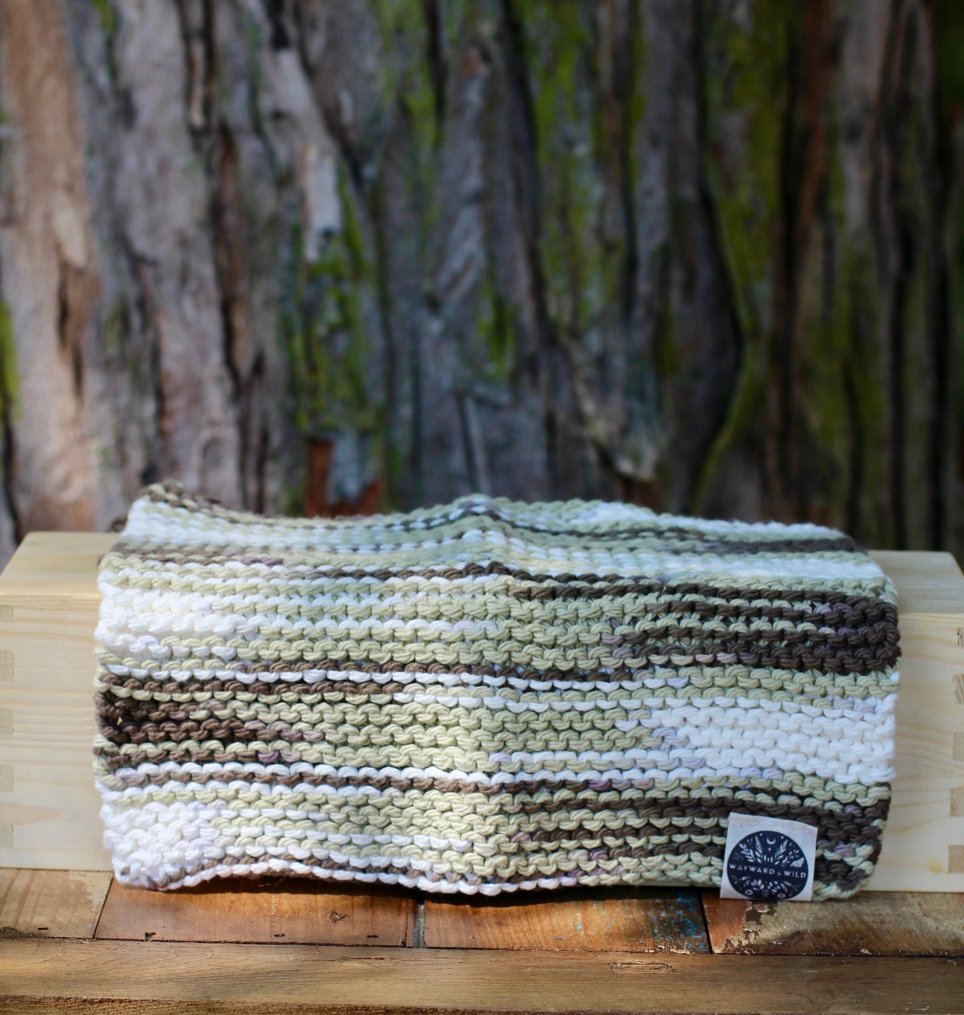 Knitted wash cloth with striped pattern on a wooden surface, blurred natural background