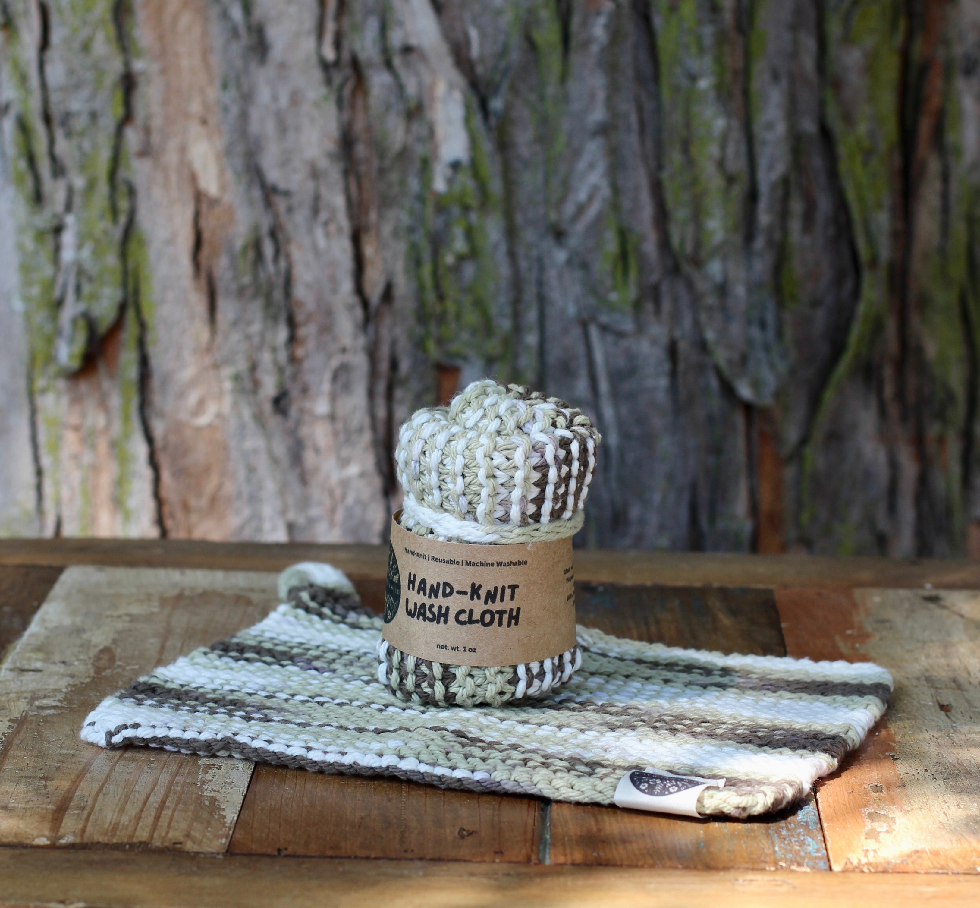 Hand-knit wash cloth in a cardboard sleeve on a wooden surface with a tree bark background