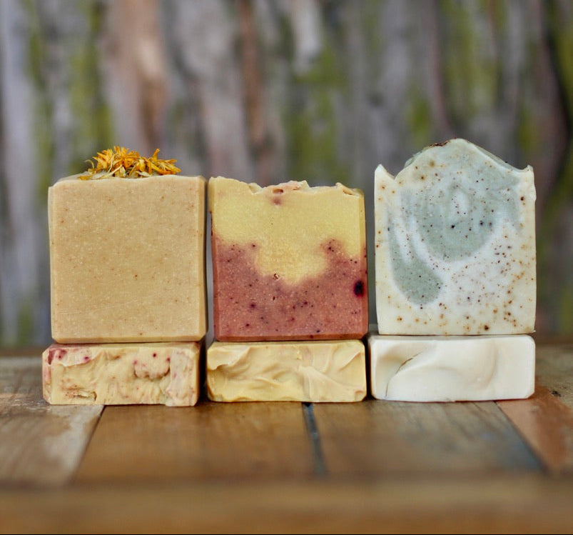 Stack of variously colored soap bars on a wooden surface with a blurred natural background